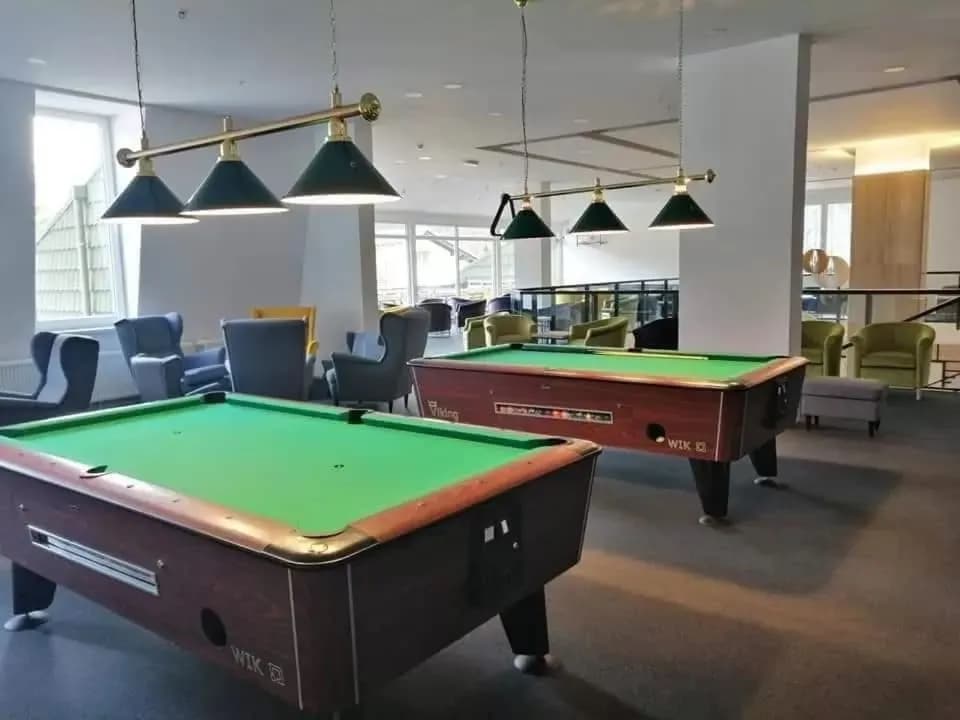 Two pool tables in the Hotel Alpina lobby lounge area with hanging brass lamps and seating.