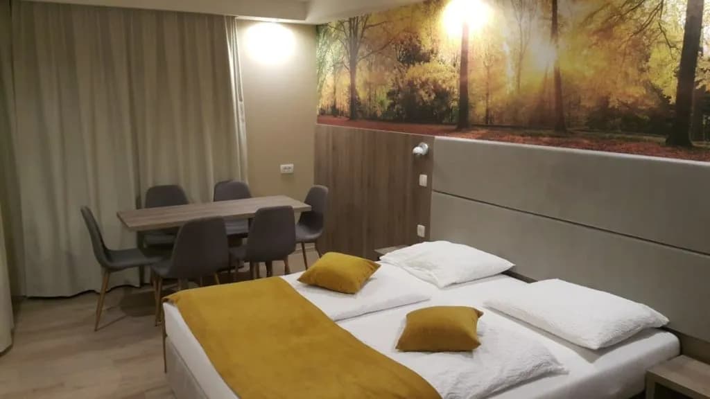 Hotel Alpina room with double bed, yellow accents, and dining table near forest mural