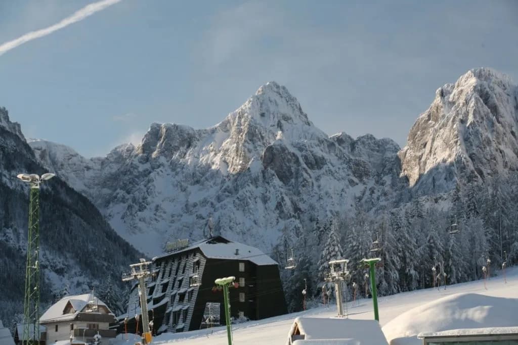 Hotel Alpina in winter with snow-covered mountains and ski lift towers.
