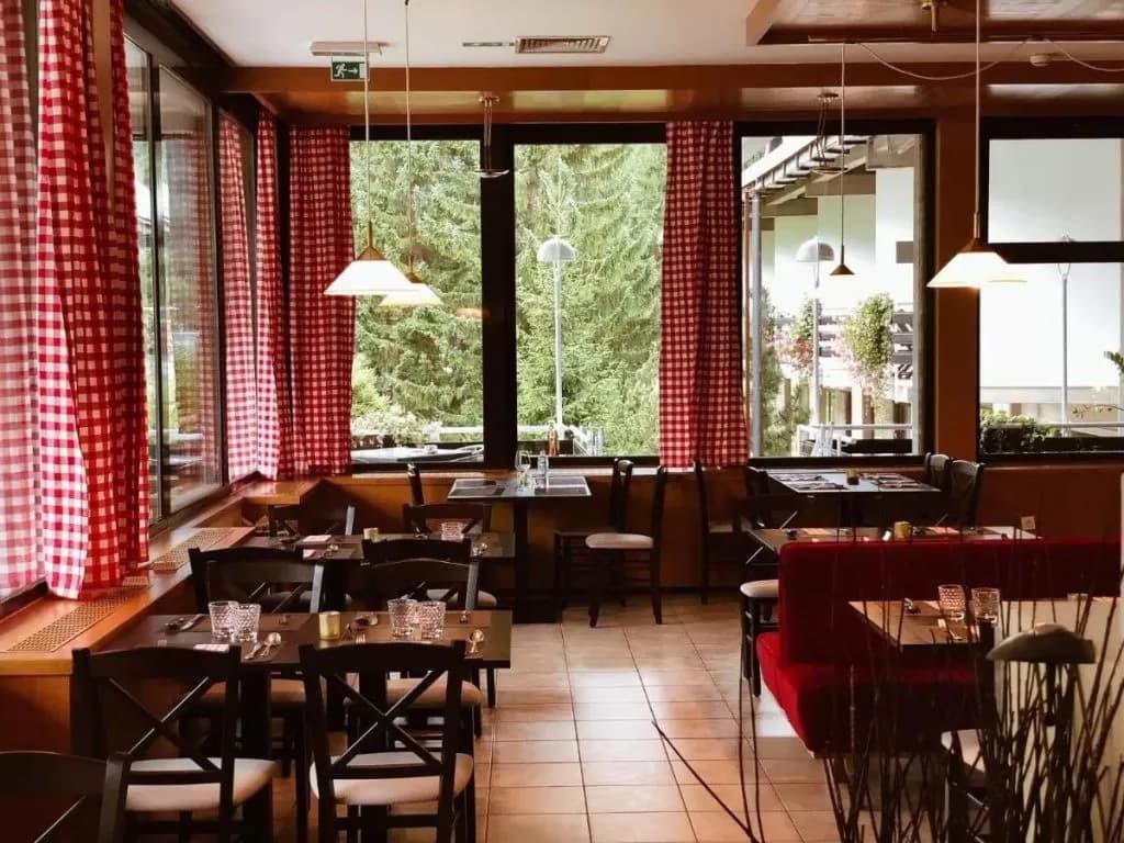 Dining area with dark wood tables, red gingham curtains, and forest view at Best Western Kranjska Gora.