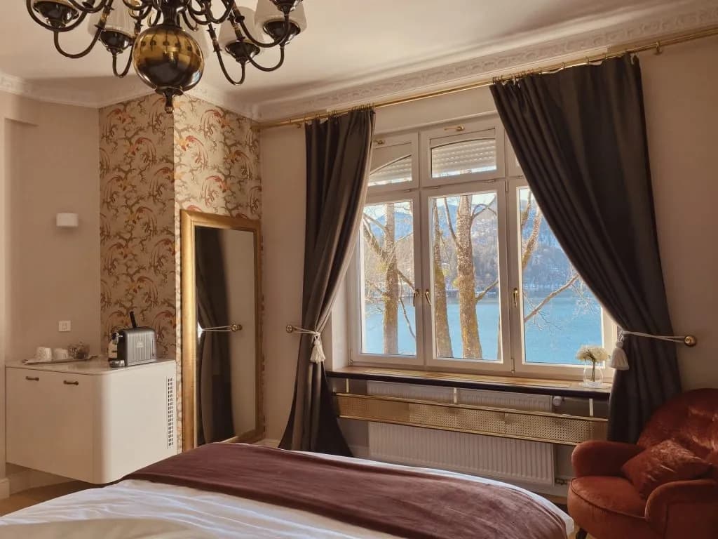 Bedroom with lake view, patterned wallpaper, and velvet armchair by window