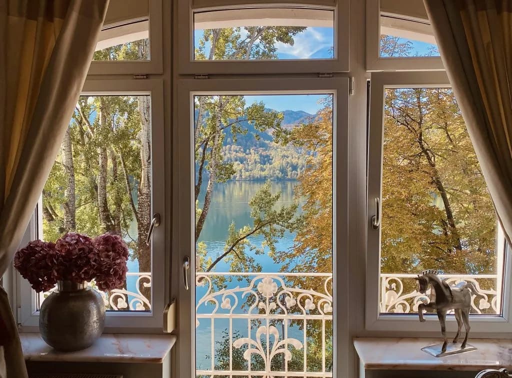 View through window with white balcony railing to lake and autumn trees on mountainside