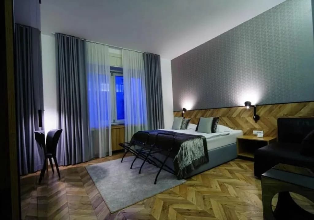 Modern hotel room with large bed, wood herringbone floor, and patterned accent wall