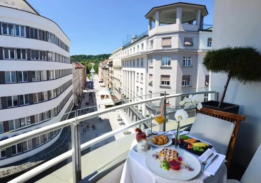 Breakfast on a hotel balcony overlooking a sunny European city street with historic buildings.