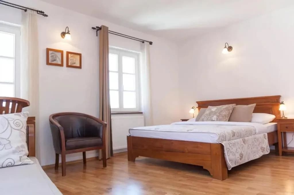 Hotel room with wooden bed, brown armchair, and light wood floor, Adora Hotel.