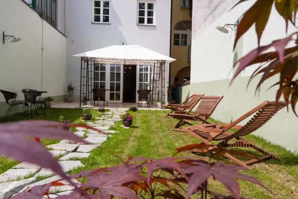 Hotel courtyard with lawn, stone path, wooden loungers, and white gazebo entrance.
