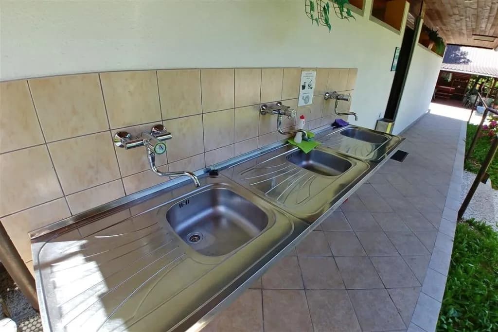 Outdoor communal stainless steel sinks with faucets against tiled wall at Vodenca campsite.