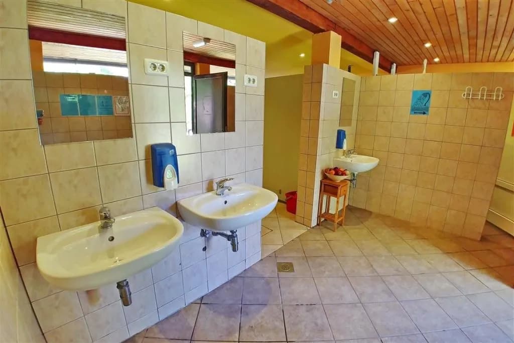 Camping Vodenca facilities: tiled washroom with multiple sinks, mirrors, and wooden ceiling.