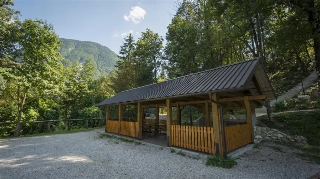 Covered wooden seating area at Vodenca campsite with forested mountain backdrop