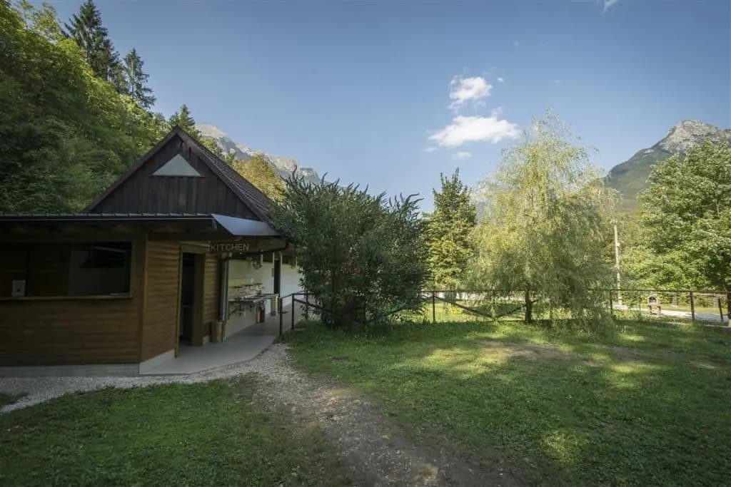 Wooden camping kitchen building with outdoor sinks surrounded by green trees and mountains.