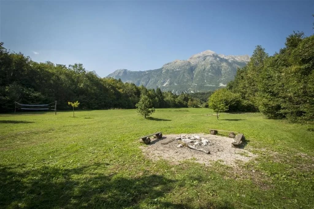 Camping area with campfire pit, volleyball net, and mountains in Vodenca on a sunny day.