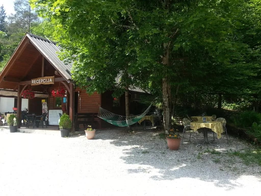 Wooden reception building with "RECEPTCIJA" sign, hammock, and outdoor seating in a wooded area.