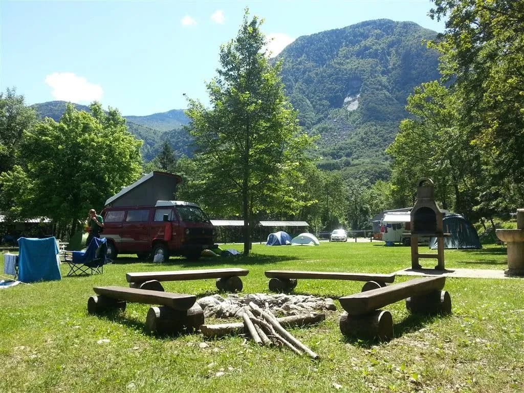 Campground with wooden benches around a fire pit, camper van, and mountains in Vodenca.