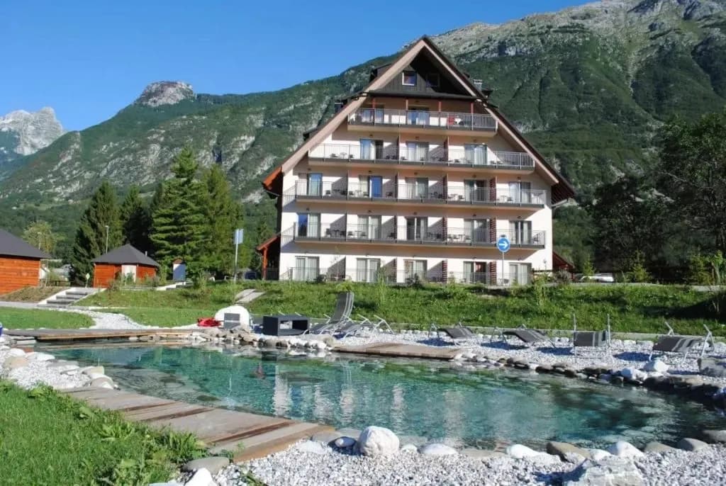 Hotel Mangart exterior with natural swimming pool and large green mountain backdrop