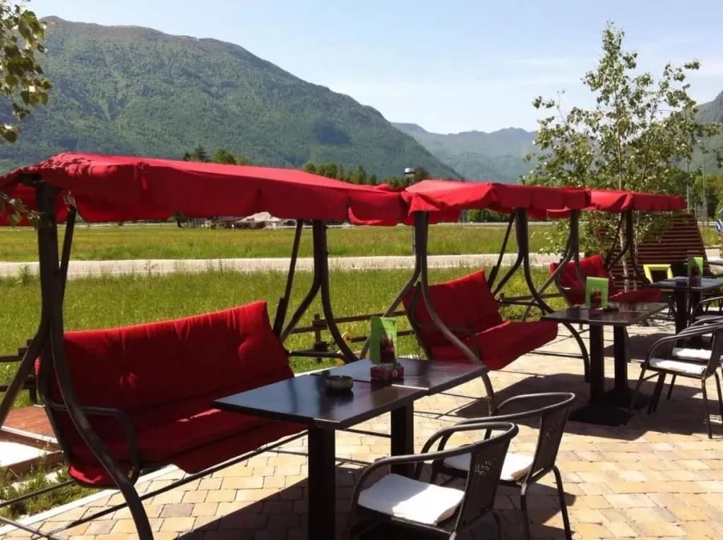 Outdoor cafe seating with red swing chairs overlooking green mountains, Hotel Mangart.
