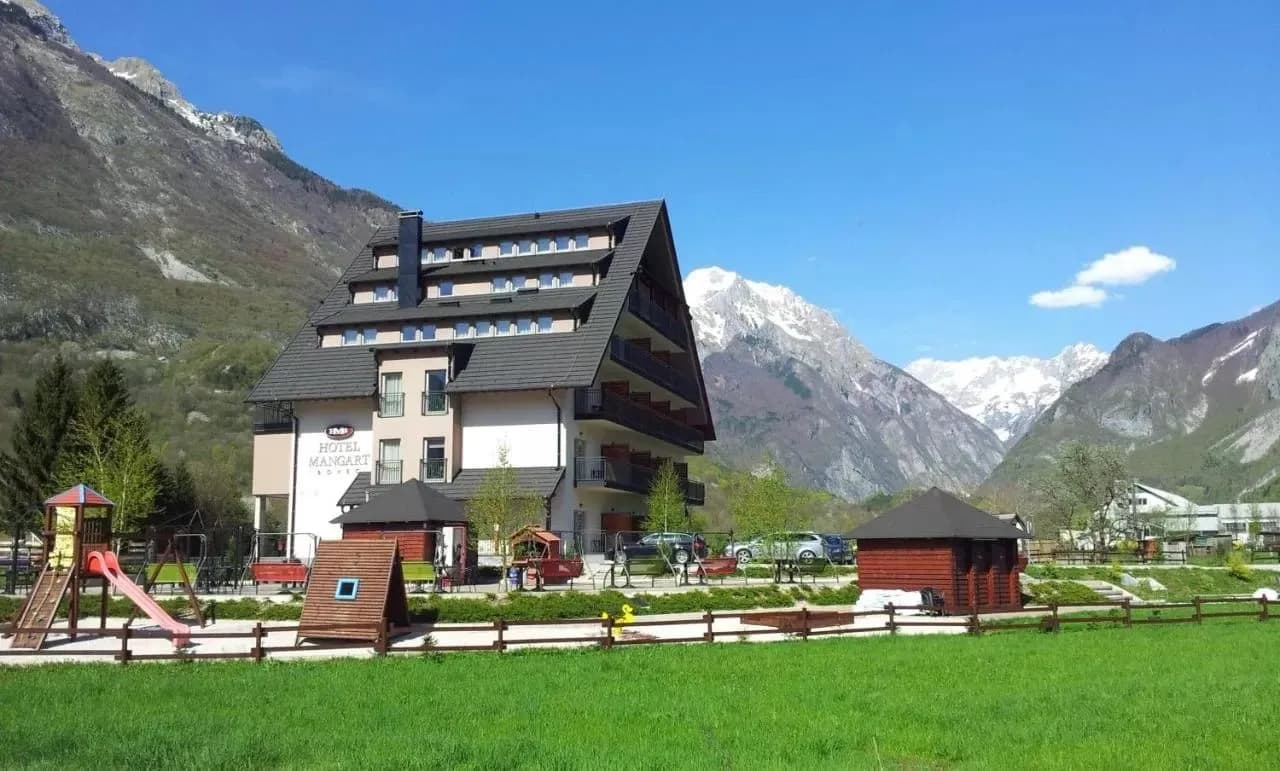 Hotel Mangart with playground in front of snow-capped mountains under a blue sky.