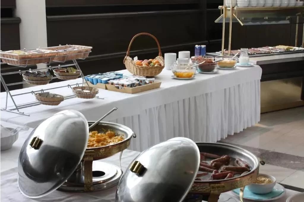 Hotel breakfast buffet with chafing dishes of scrambled eggs and sausages, fruit, and yogurt.