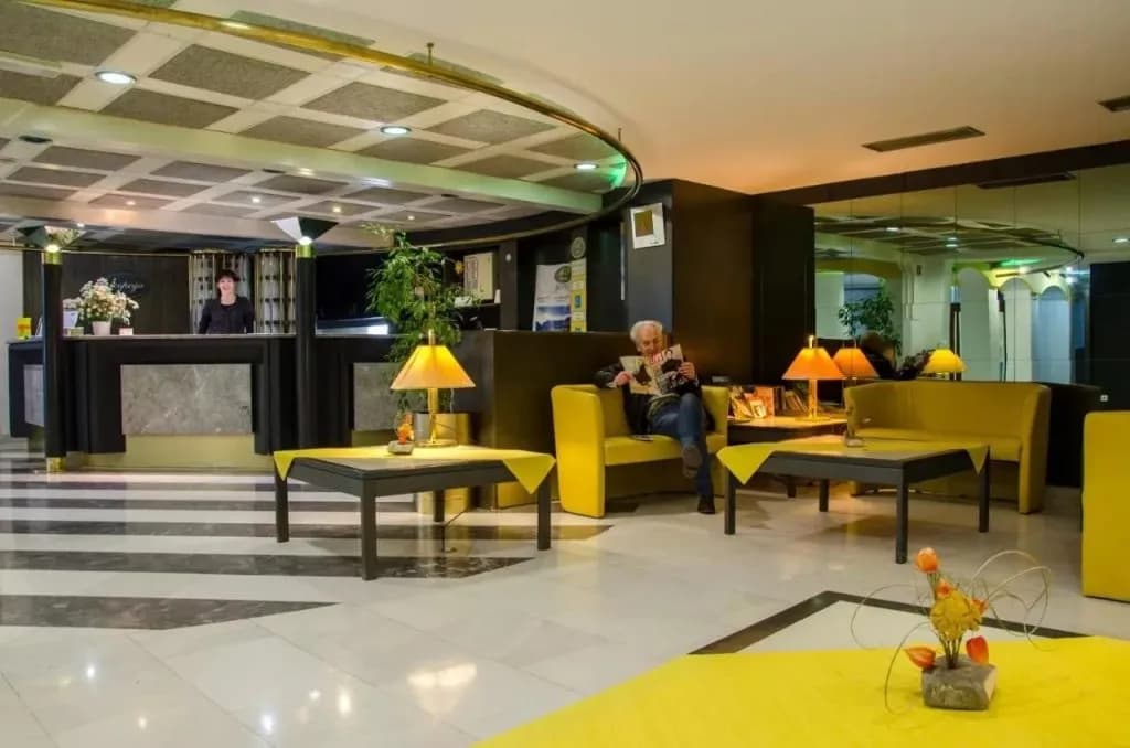Hotel reception area with black and yellow decor, a man reading, and a staff member at the desk.