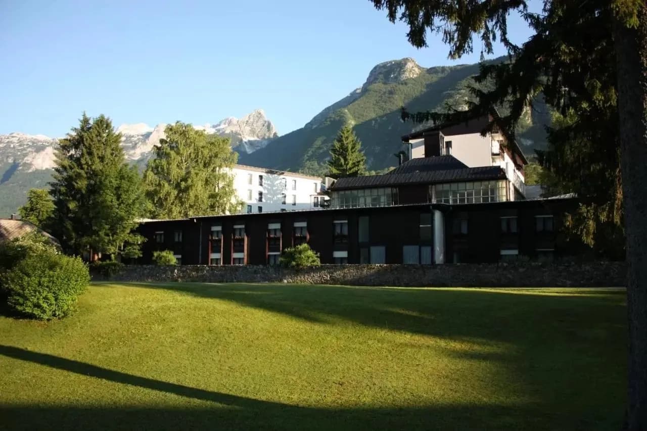 Alpine hotel exterior with dark wood and white sections set against green lawn and mountains.