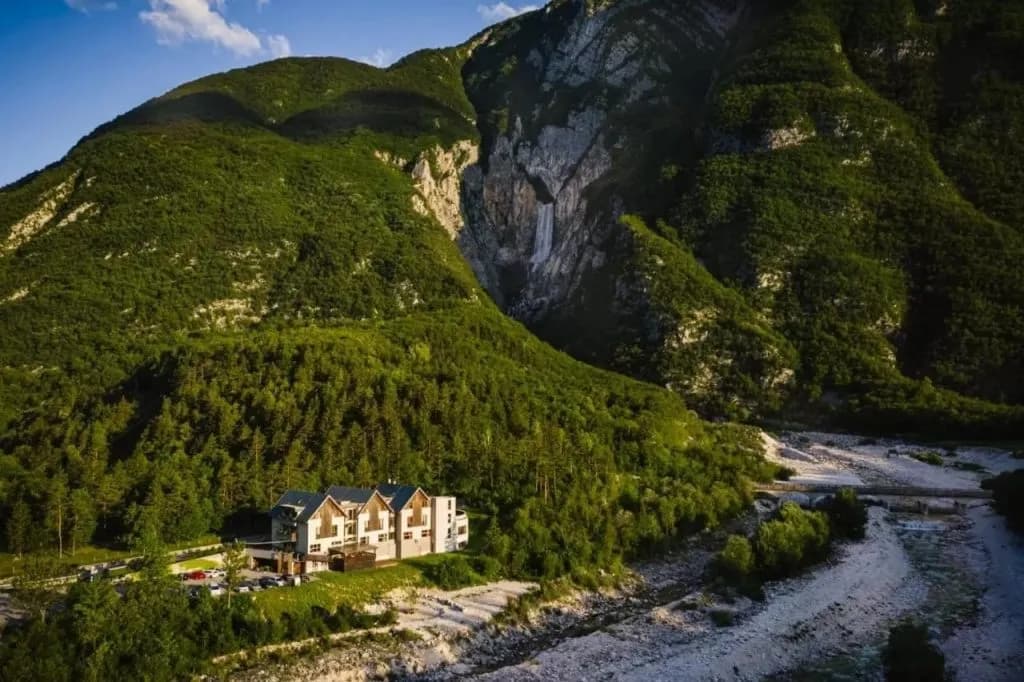 Hotel near Boka Waterfall nestled in a lush green mountain valley beside a rocky riverbed.
