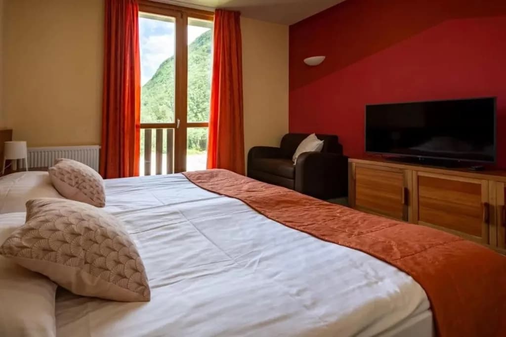 Hotel room with large bed, TV, and balcony view of green mountains