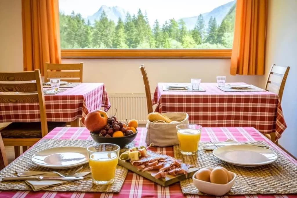 Breakfast spread with fruit, meat, and juice overlooking forested mountains through a window.