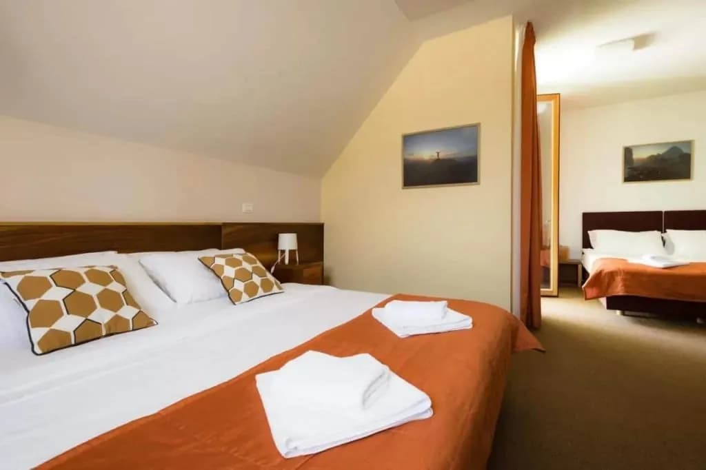 Hotel room with large bed, orange accents, and view into a second sleeping area