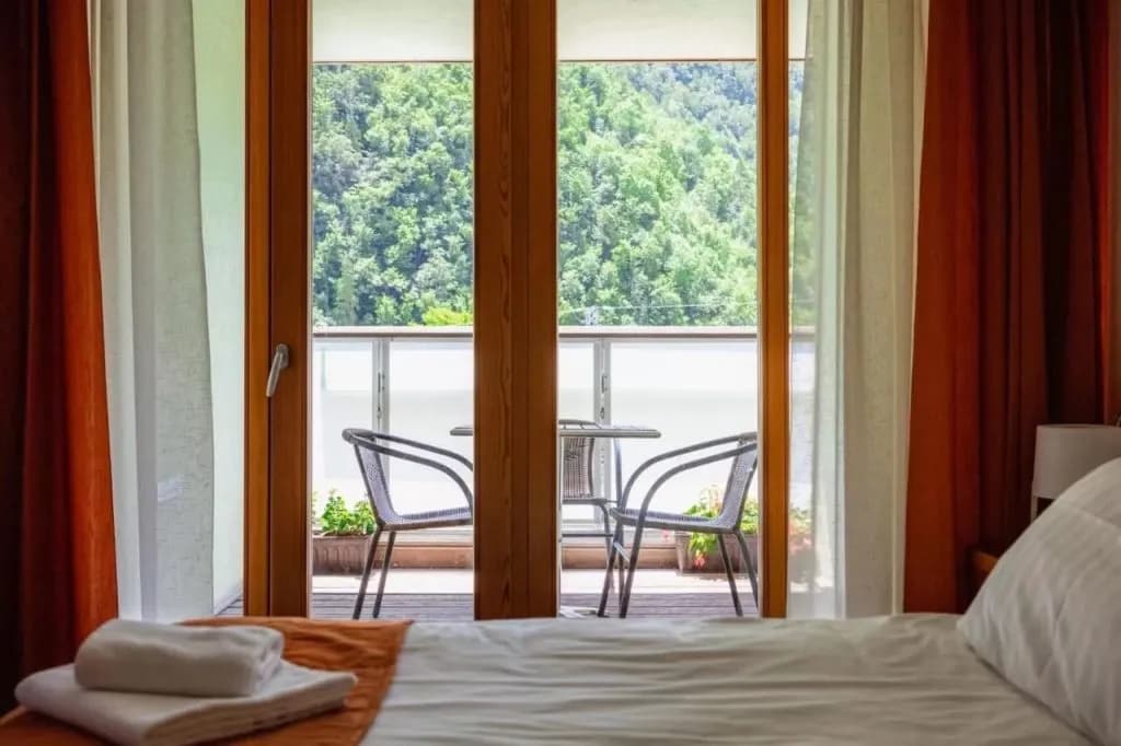 Hotel room balcony with chairs overlooking lush green forested mountainside