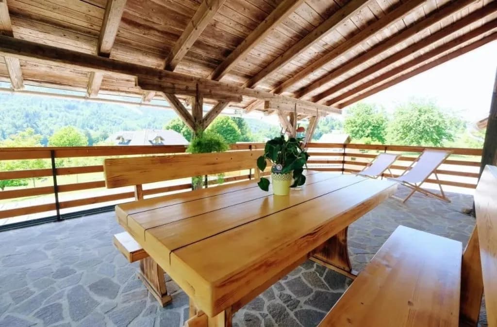 Covered wooden seating area with large table overlooking green hills at Glamping Zgornja Dobrava.