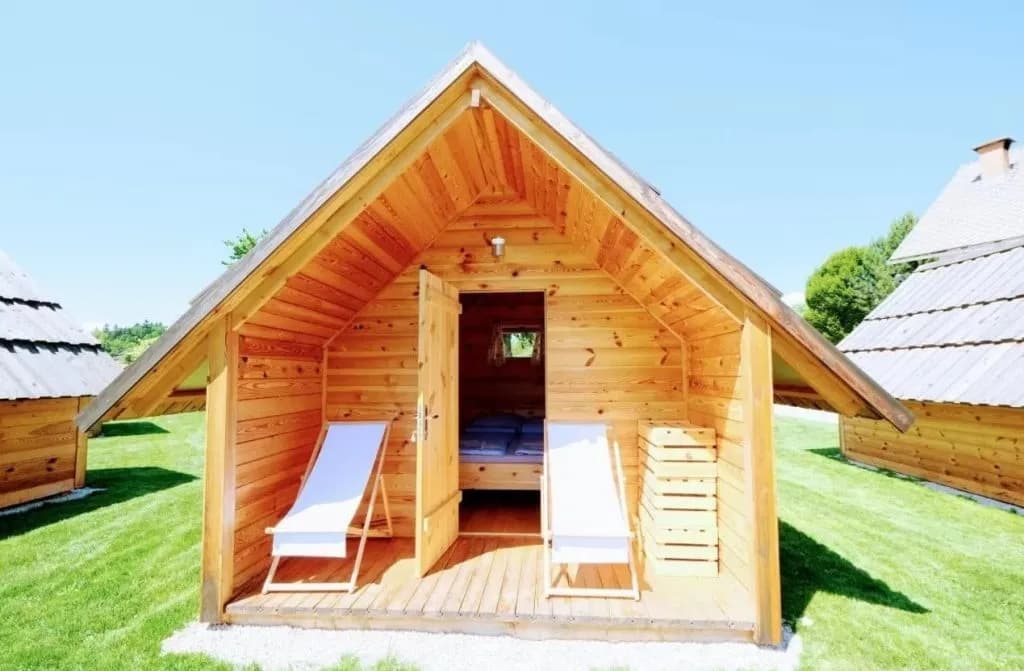 Wooden glamping cabin with open door, deck chairs, and green lawn in Zgornja Dobrava.
