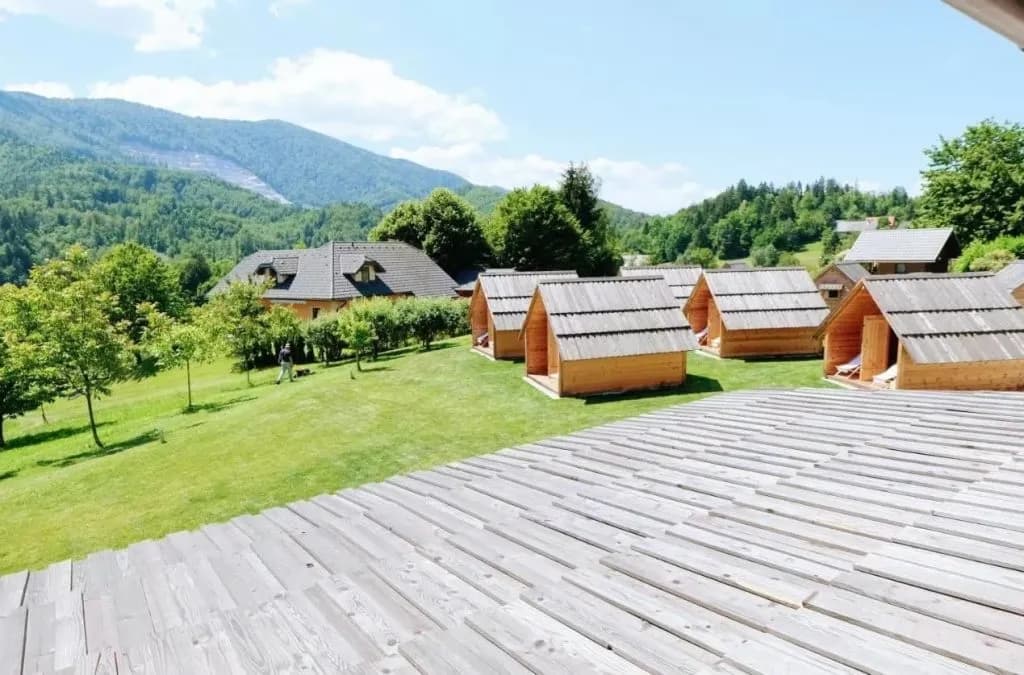 Glamping cabins on grassy slope with wooden deck and forested mountains in Zgornja Dobrava.
