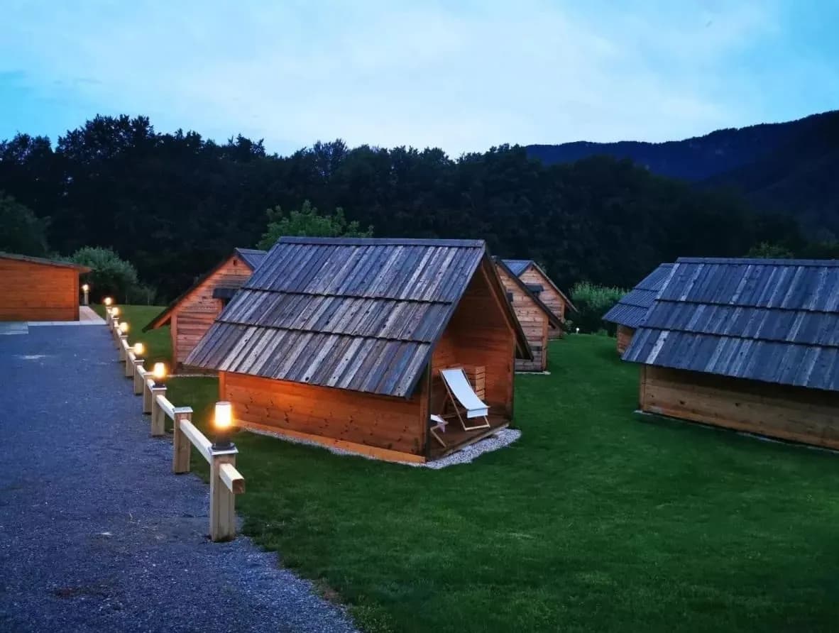 Wooden glamping cabins with shingled roofs at dusk near forested mountains in Zgornja Dobrava.