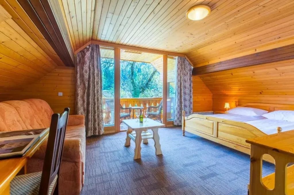 Penzion Berc room with wooden paneling, double bed, and balcony overlooking trees.