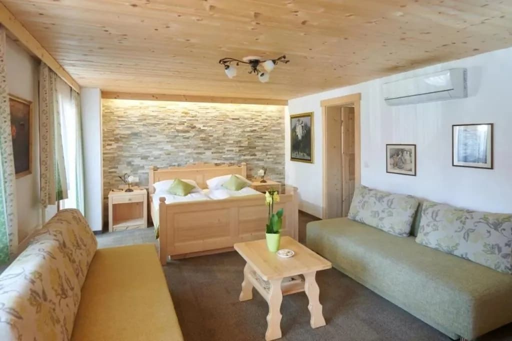 Penzion Berc suite bedroom with wooden furniture, stone accent wall, and light green sofas.
