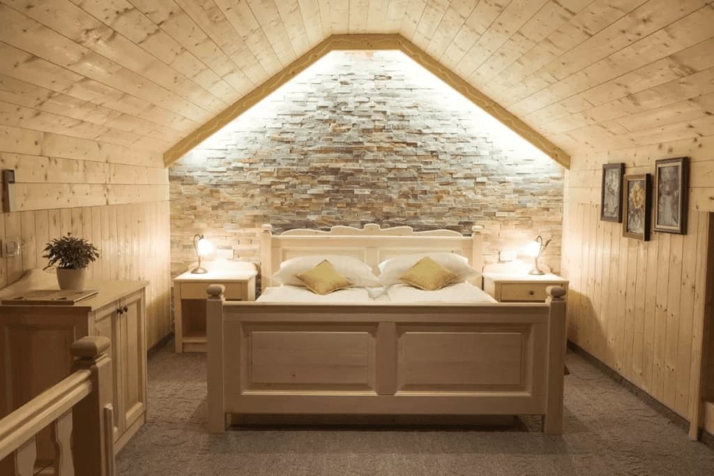 Attic bedroom with light wood paneling, stone accent wall, and white wooden bed frame.
