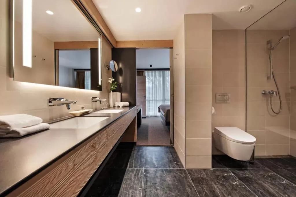 Modern bathroom with double vanity, dark marble floor, and view into a bedroom.