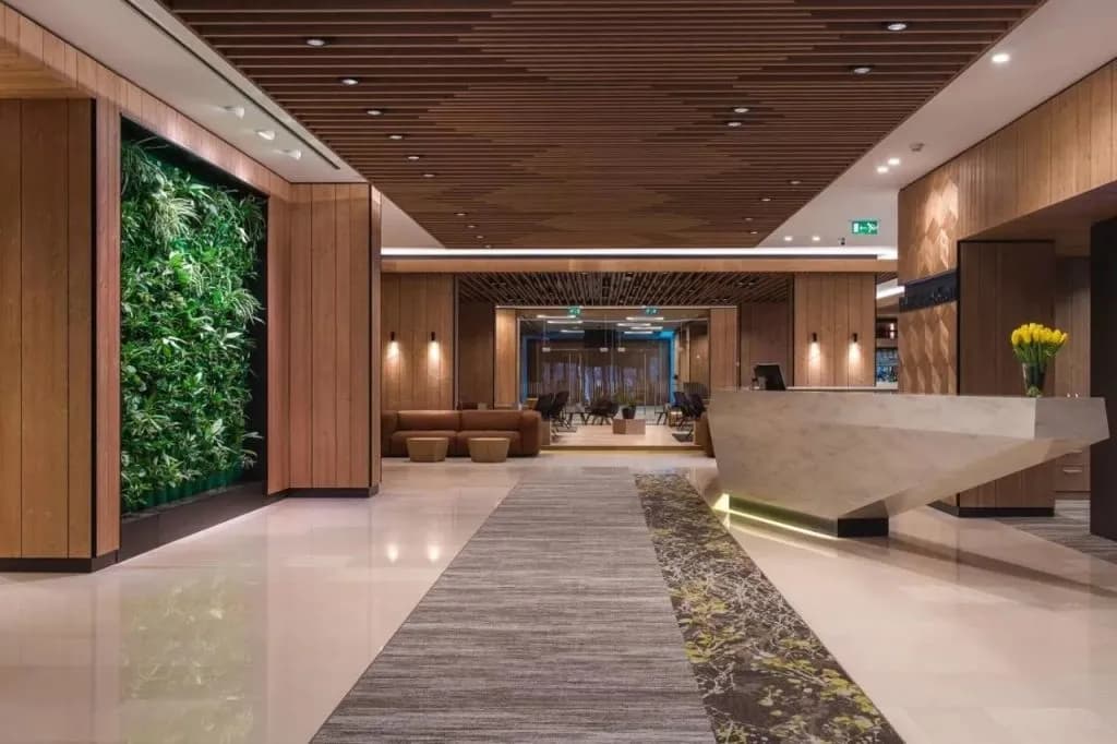 Modern hotel reception area with wood paneling, a vertical garden, and a geometric desk.