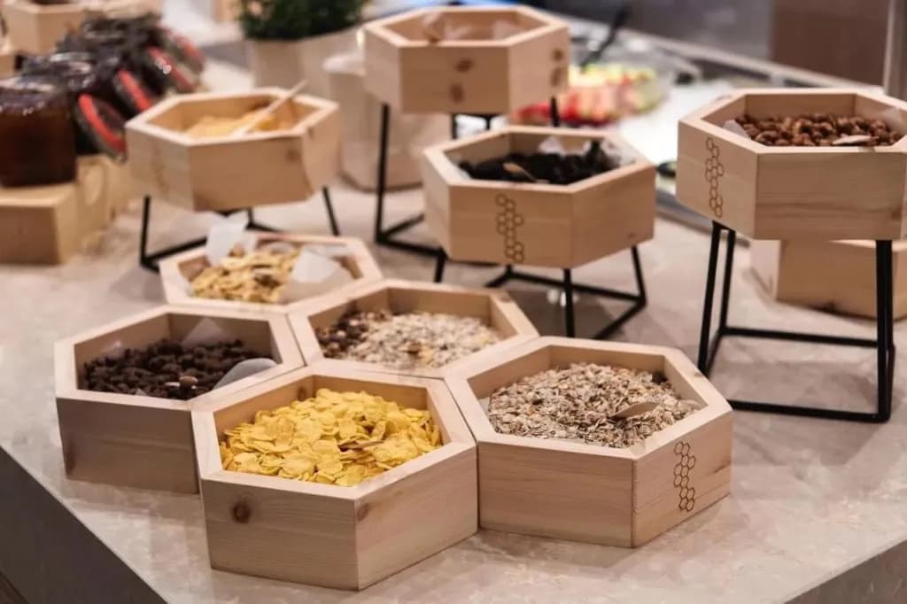 Cereal and granola displayed in hexagonal wooden containers at a breakfast buffet.