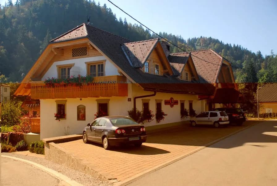 Garni-Hotel Berc with wooden balcony parked cars against forested mountain backdrop