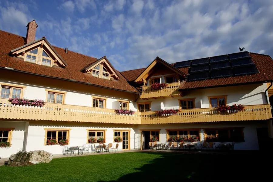 Garni Hotel Berc with white facade, wooden balconies, and green lawn under blue sky