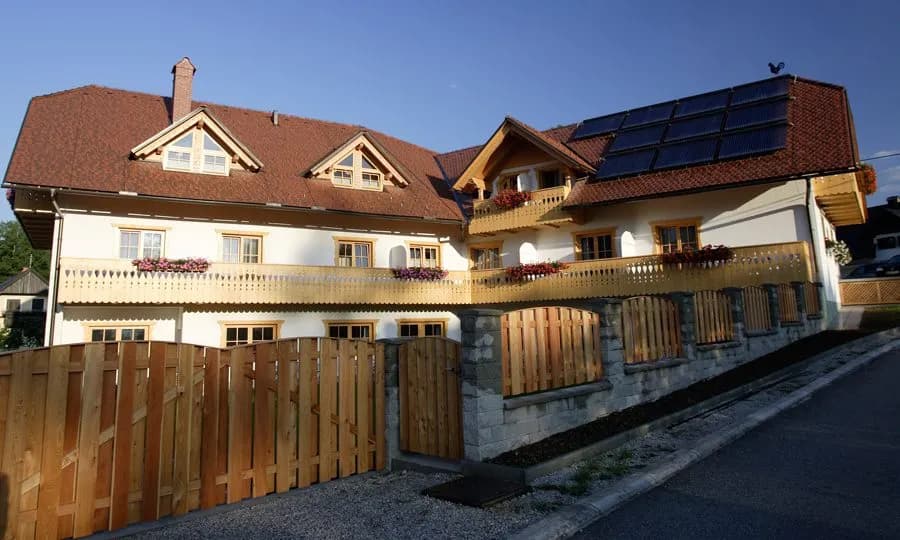 Garni Hotel Berc with white facade, wooden balconies, and solar panels under blue sky.
