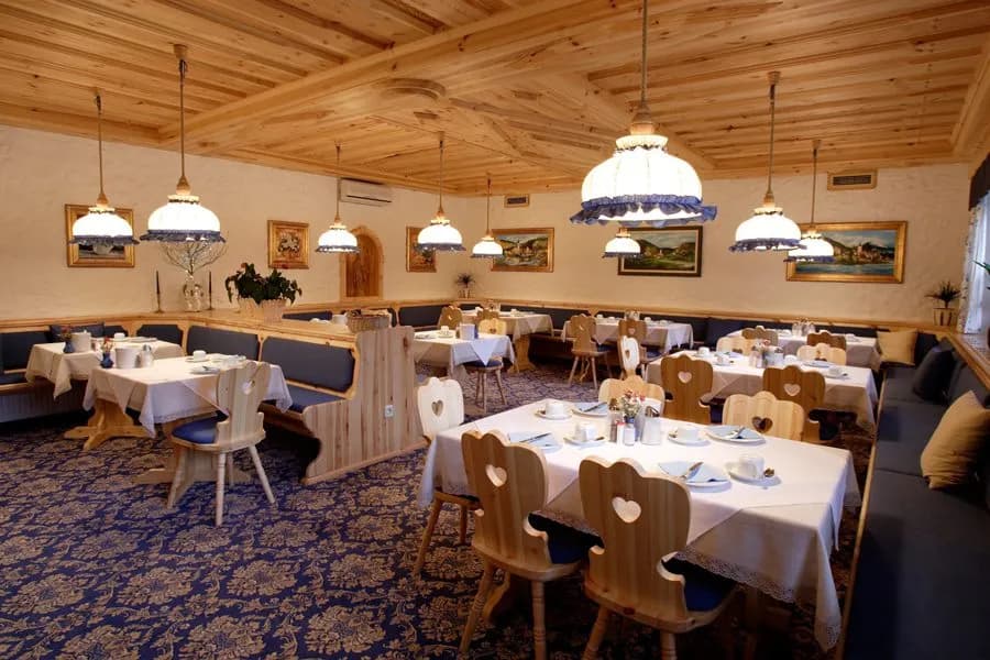 Dining area with wood paneling, heart-backed chairs, and blue patterned carpet at Garni Hotel Berc.