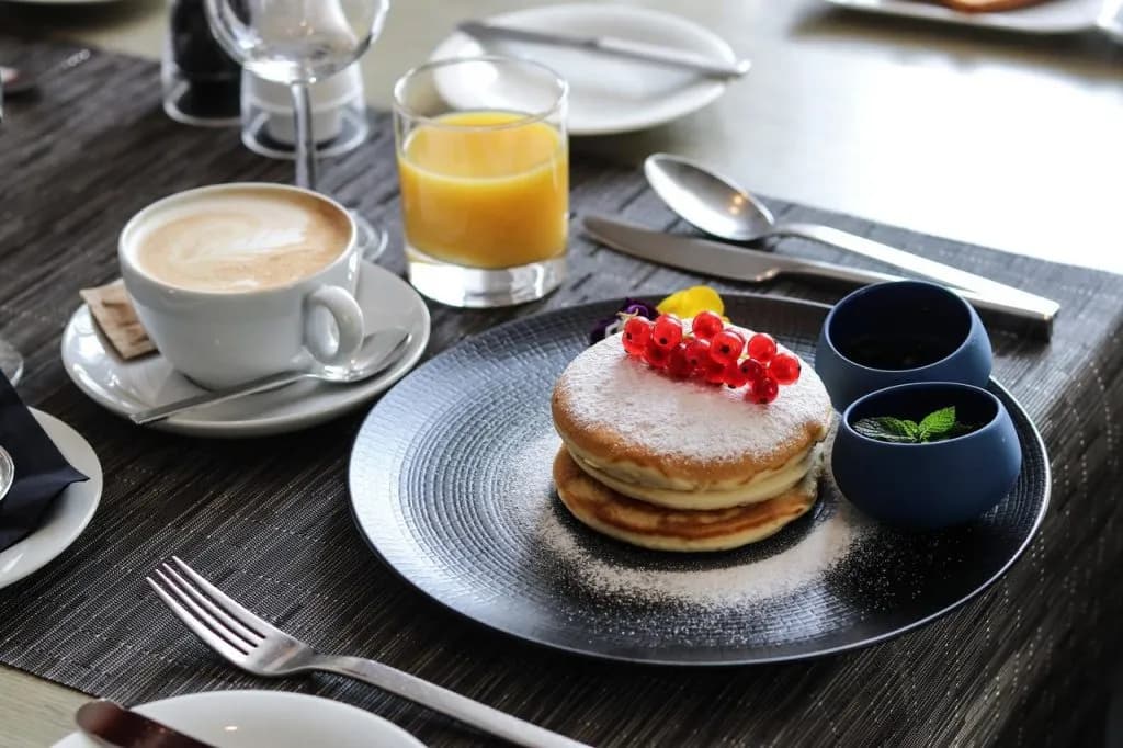 Pancakes dusted with powdered sugar and red currants served with coffee and orange juice at hotel breakfast.