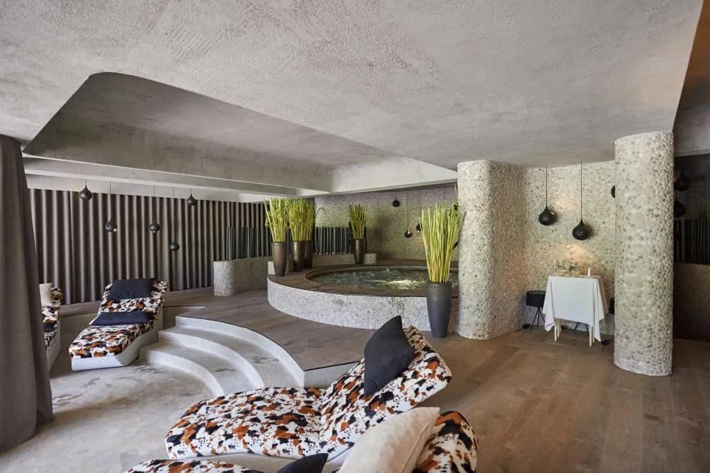 Indoor spa area with circular hot tub, lounge chairs, and pebble-textured columns at Hotel Plesnik