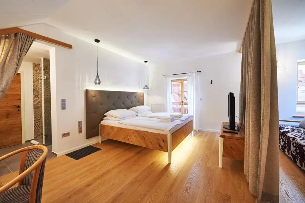 Hotel Plesnik room with wood floor, white walls, and modern floating bed with tufted headboard.