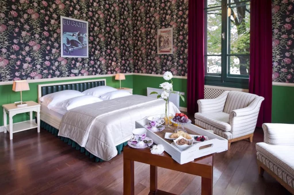 Boutique hotel room with floral wallpaper, white bedding, and breakfast tray on a dark wood floor.