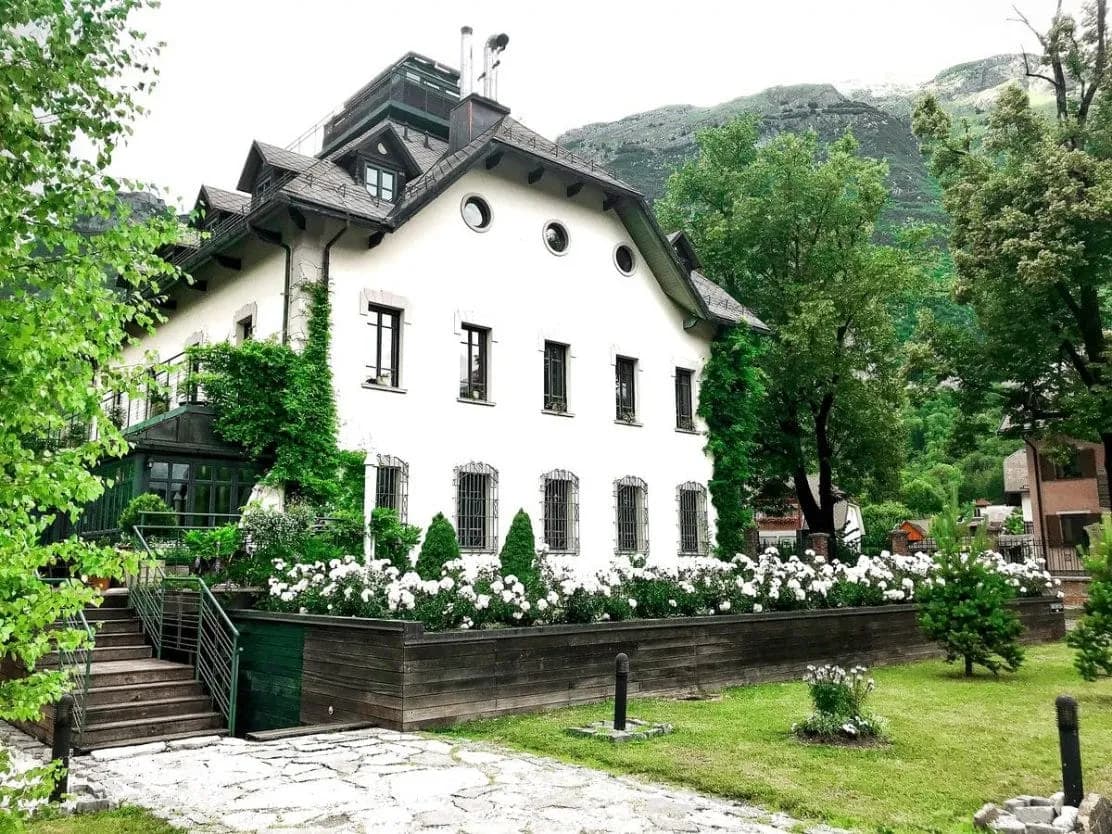 Boutique Hotel Dobra Vila building with white facade, white roses, and lush green mountains in background.