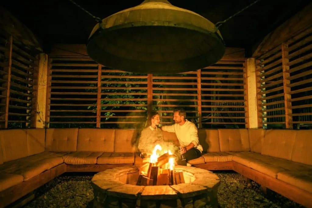 Couple relaxing by outdoor stone fire pit under large metal hood in Garden Village Bled.