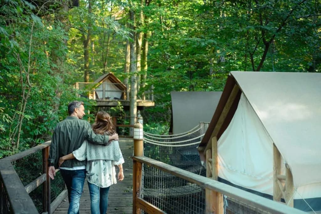 Couple walking on wooden walkway past glamping tents in lush green forest near Bled.