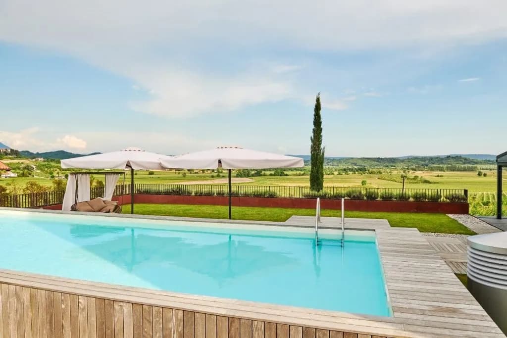 Infinity pool with wooden deck overlooking green rolling hills and distant mountains